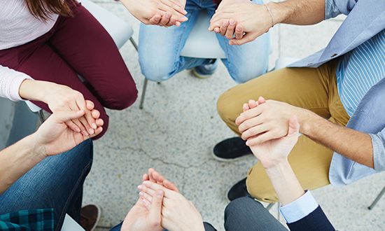 Group of students holding by hands while sitting in circle