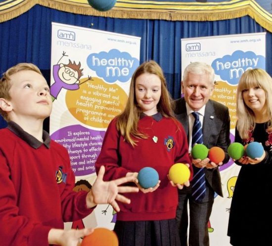 Two children juggling balls and an adult couple assisting them.