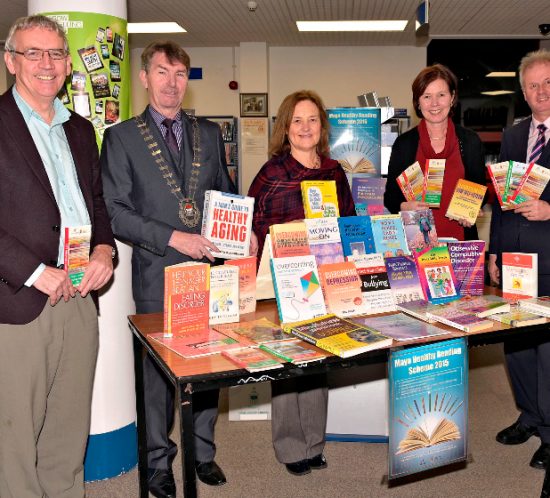 A group of people presenting books, and standing behind a table covered with a large amount of various books.