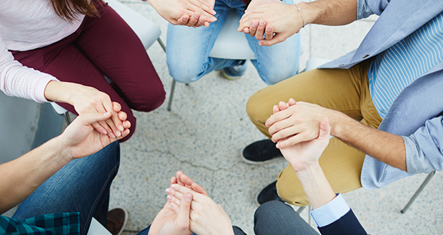 Group of students holding by hands while sitting in circle