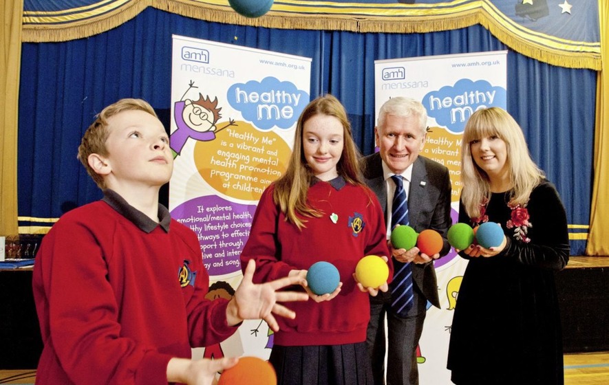 Two children juggling balls and an adult couple assisting them.